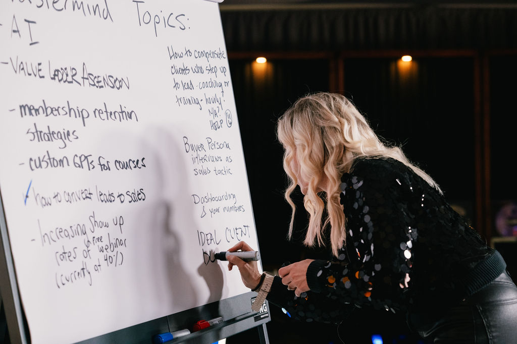Sarah writing strategy notes on a whiteboard during a live mastermind